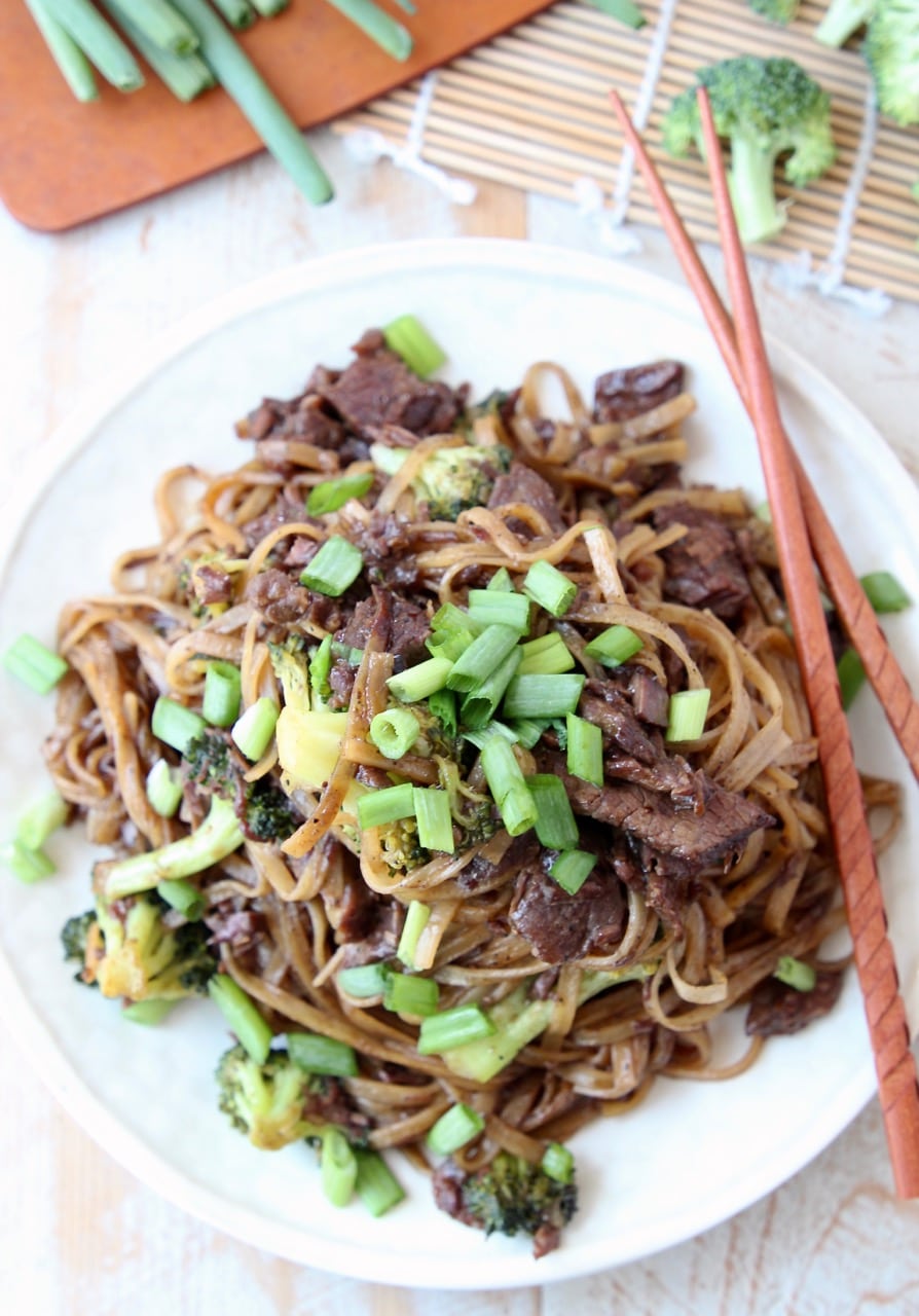 Beef and broccoli with rice noodles and scallions on plate with chopsticks