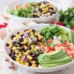 White bowl with sliced avocado, black bean and corn relish, diced tomatoes and shredded lettuce