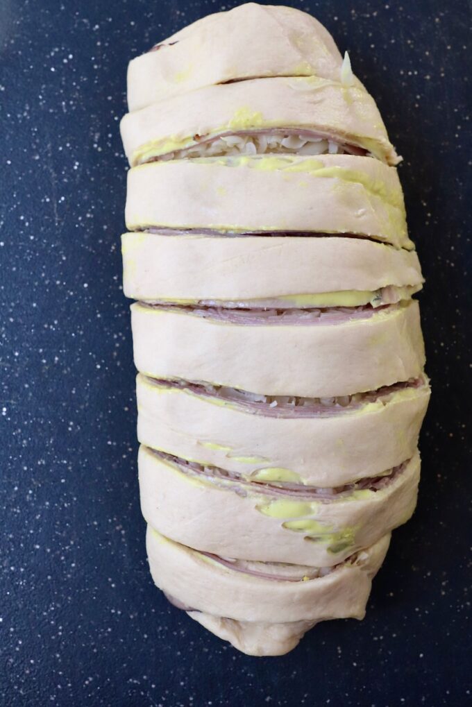 crescent roll dough rolled up over ham and swiss, sliced in one inch sections on a cutting board