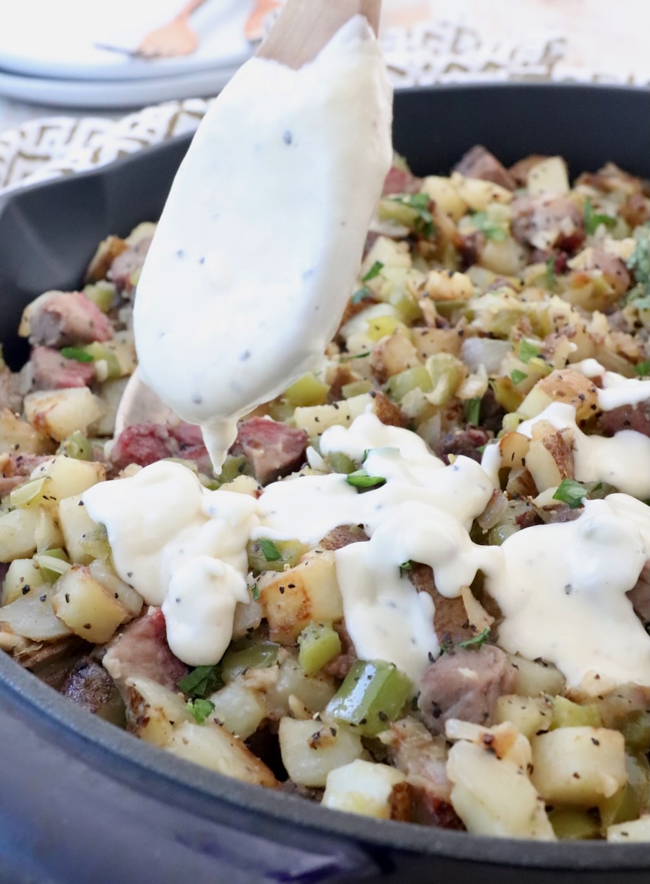 cheese sauce in spoon drizzled over potato hash in skillet