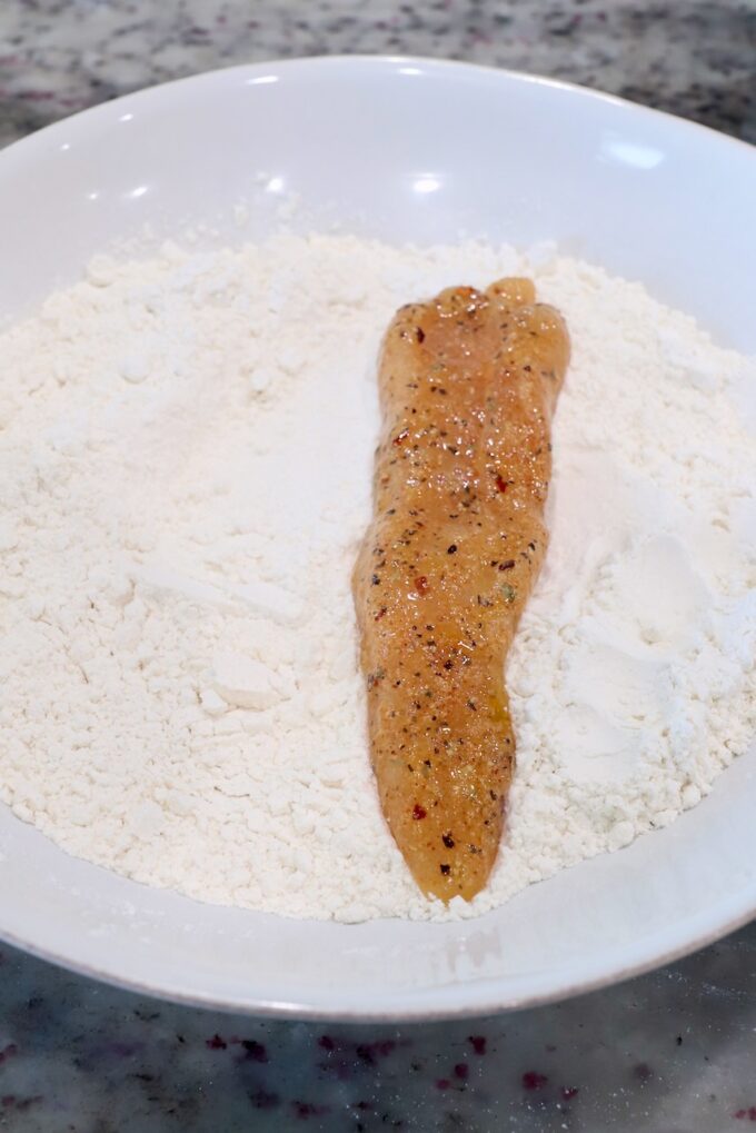 strip of seasoned chicken  in bowl of flour