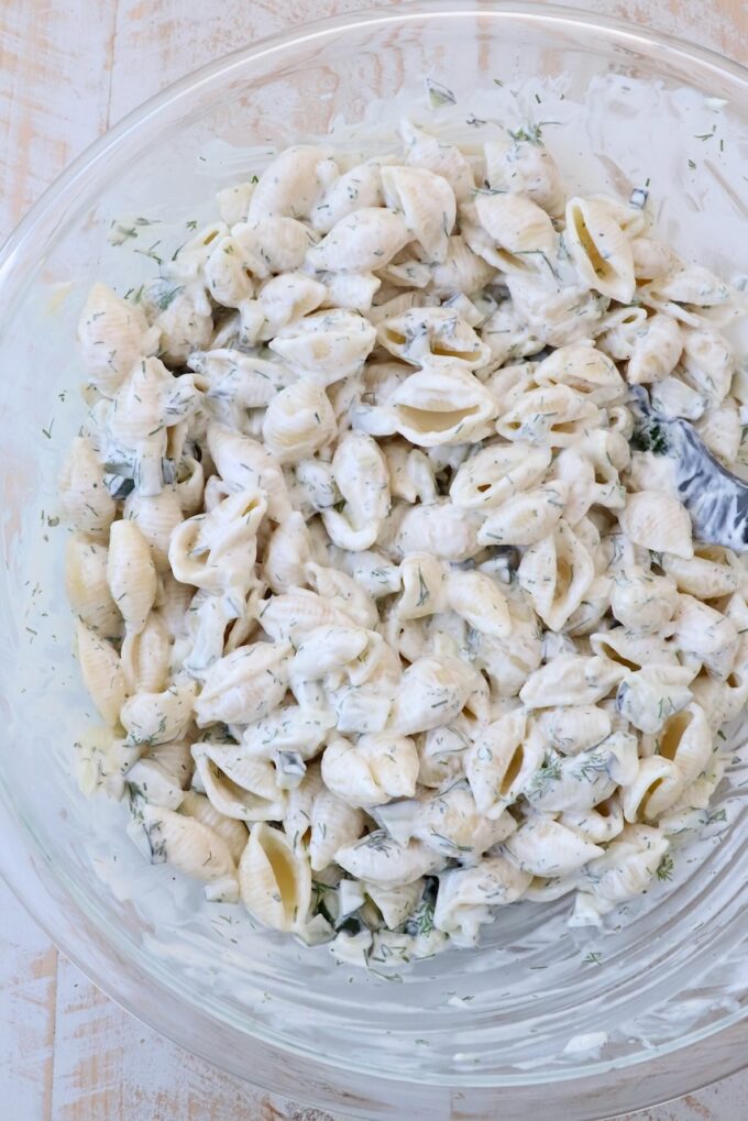 pickle pasta salad ingredients mixed together in large glass bowl