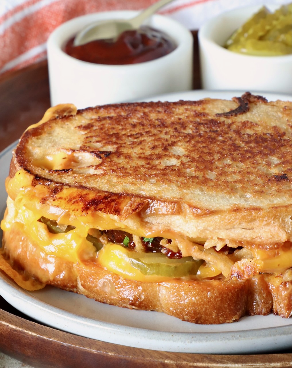 meatloaf sandwich on a plate with a small bowl of bbq sauce and small bowl of pickles behind the sandwich
